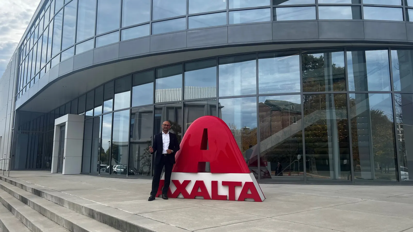 Enzo Santarsiero steht neben einer grossen roten Axalta-Skulptur vor einer Glasfassade