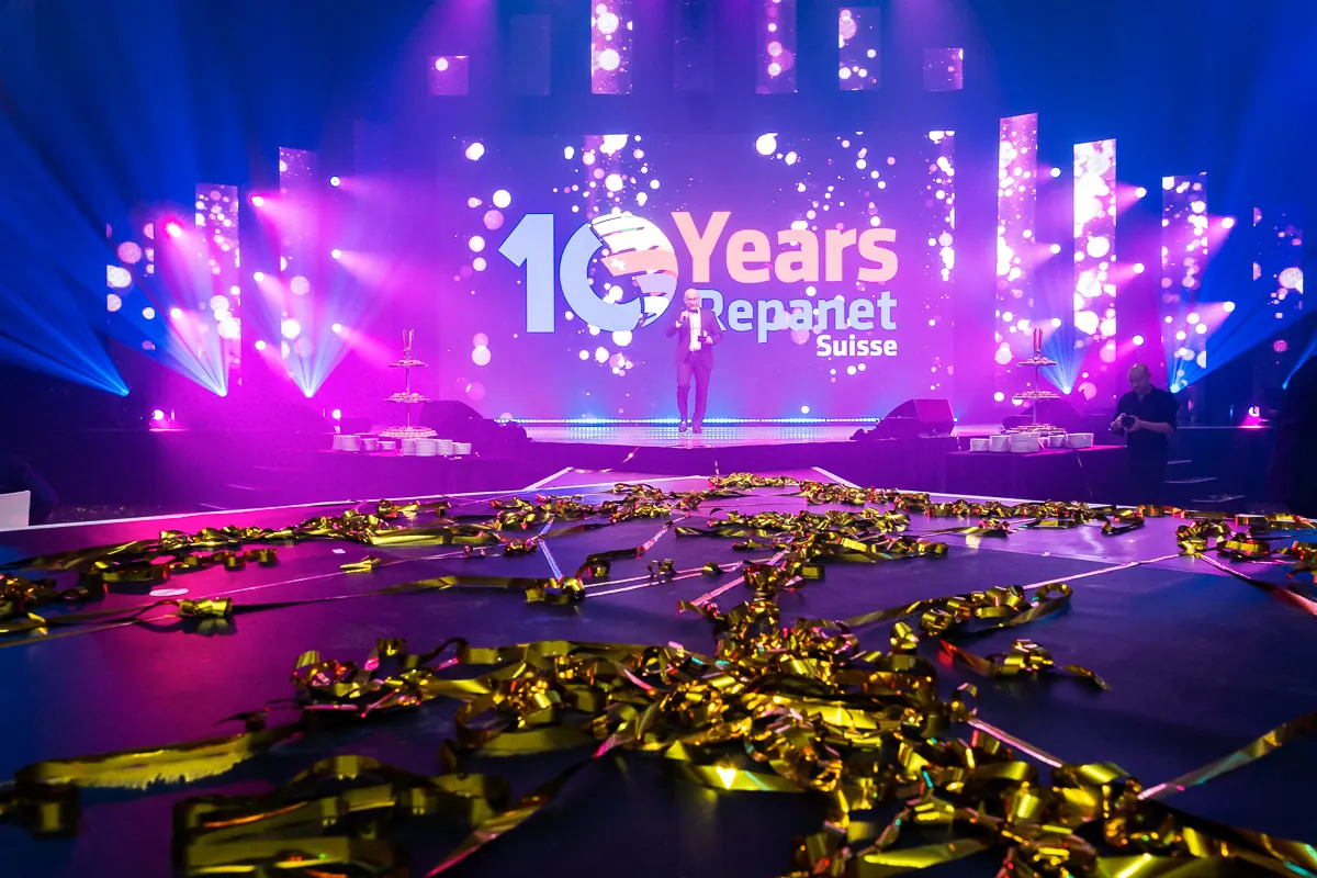 Bühne mit „10 Years Repanet Suisse“-Leinwand, im Vordergrund goldenes Konfetti